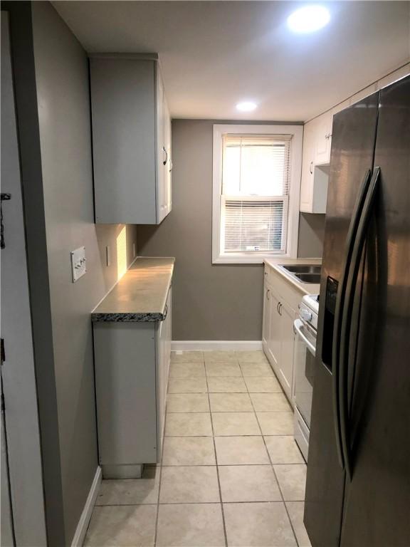 kitchen with light tile patterned floors, sink, white cabinetry, white range, and black fridge with ice dispenser