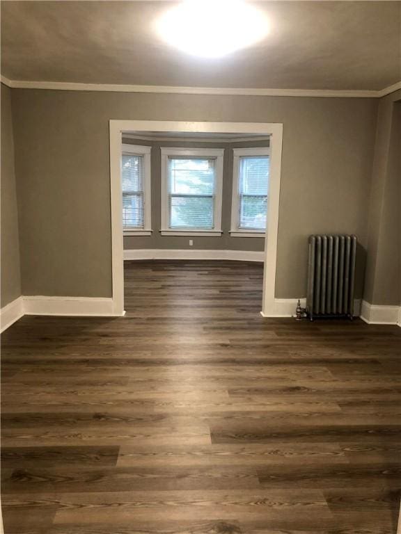 empty room with radiator, crown molding, and dark wood-type flooring