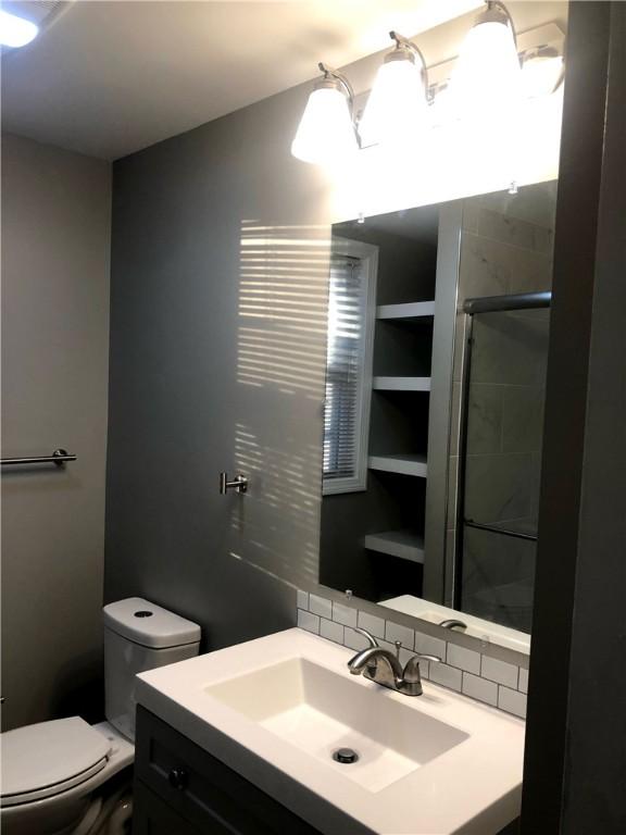 bathroom featuring vanity, toilet, a shower with shower door, and decorative backsplash