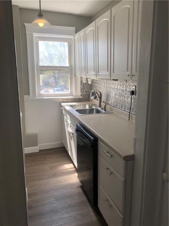 kitchen with hardwood / wood-style floors, white cabinetry, black dishwasher, sink, and hanging light fixtures