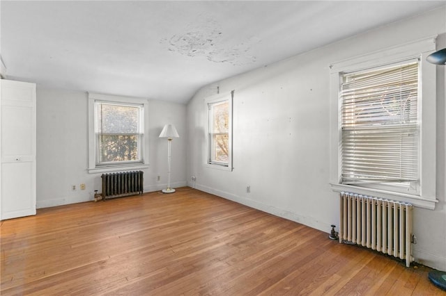 unfurnished living room featuring radiator, vaulted ceiling, and light wood-type flooring