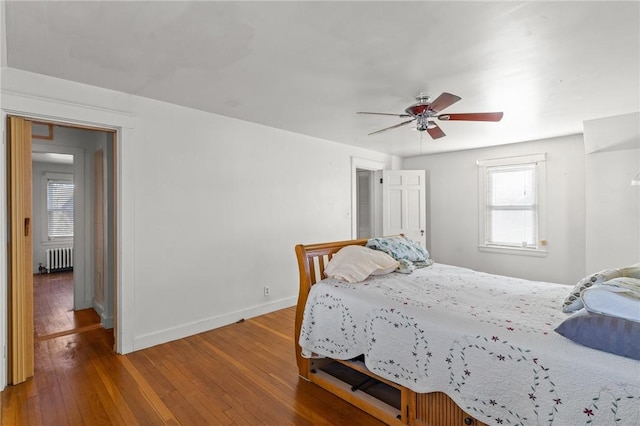 bedroom with ceiling fan, radiator heating unit, hardwood / wood-style floors, and multiple windows