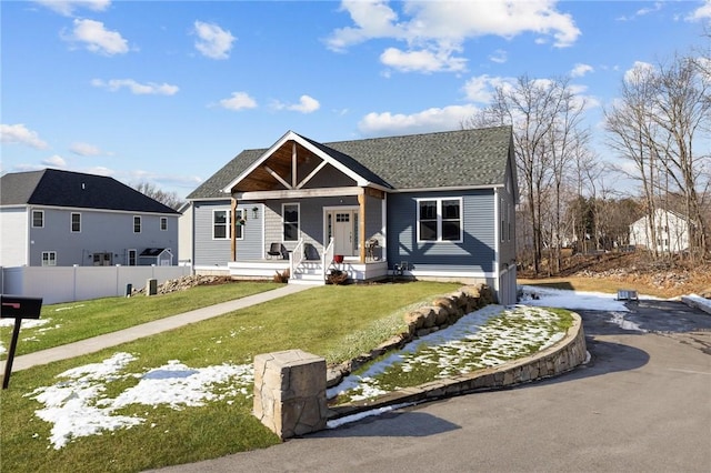 view of front of home with covered porch, a front lawn, and fence