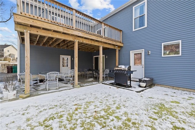 snow covered house featuring a wooden deck and a patio