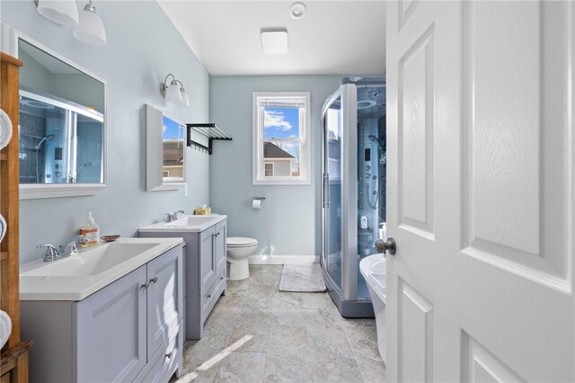 bathroom featuring a shower stall, two vanities, baseboards, and a sink