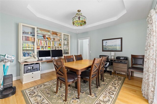 dining room with baseboards, a raised ceiling, and light wood-style floors