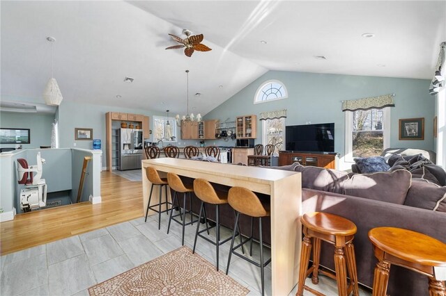 kitchen featuring pendant lighting, a breakfast bar, stainless steel refrigerator with ice dispenser, open floor plan, and vaulted ceiling