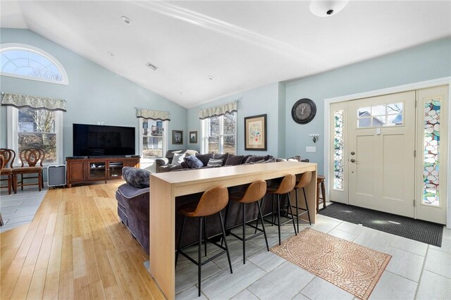 living room featuring light wood finished floors, visible vents, a healthy amount of sunlight, and vaulted ceiling