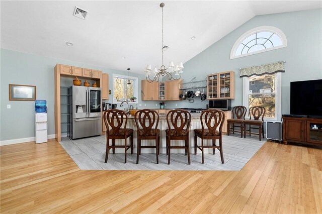 dining space featuring baseboards, visible vents, light wood finished floors, high vaulted ceiling, and an inviting chandelier