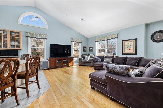 living room with visible vents, light wood-type flooring, and high vaulted ceiling