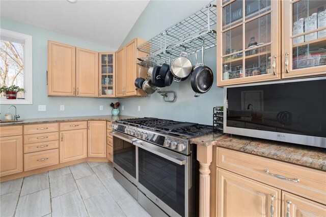 kitchen with light brown cabinets, light stone counters, range with two ovens, glass insert cabinets, and vaulted ceiling