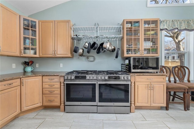 kitchen with light brown cabinetry, lofted ceiling, stone counters, and range with two ovens