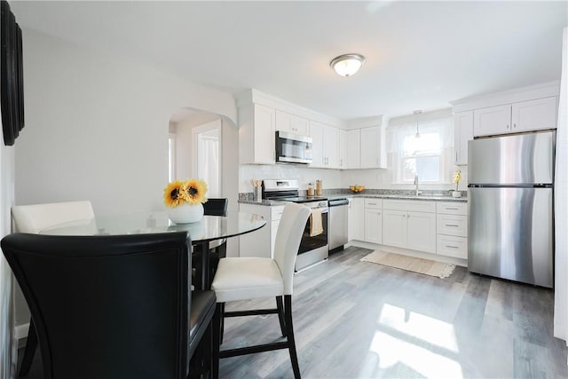 kitchen featuring white cabinetry, sink, light stone counters, light hardwood / wood-style floors, and stainless steel appliances