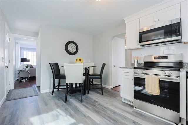 kitchen with backsplash, stainless steel appliances, light stone countertops, and white cabinets