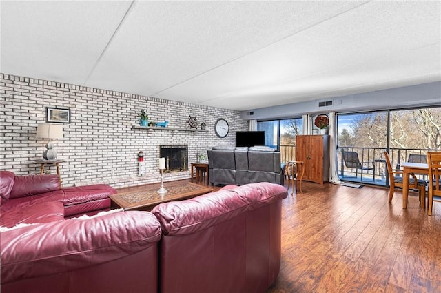 living room featuring dark wood-type flooring, brick wall, a brick fireplace, and a textured ceiling