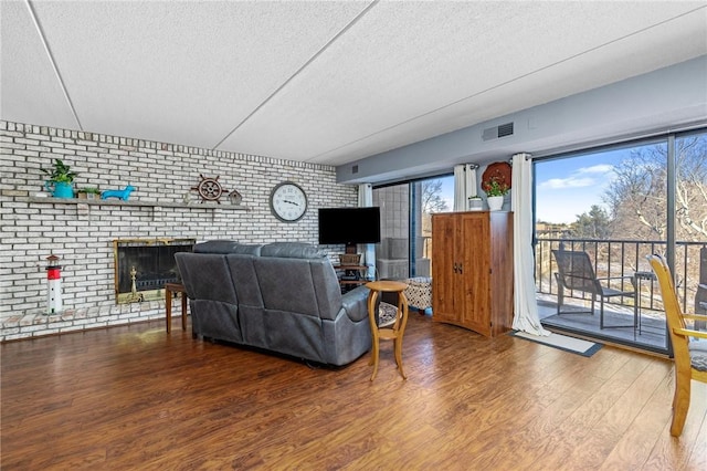 living room with brick wall, wood-type flooring, a fireplace, and a textured ceiling