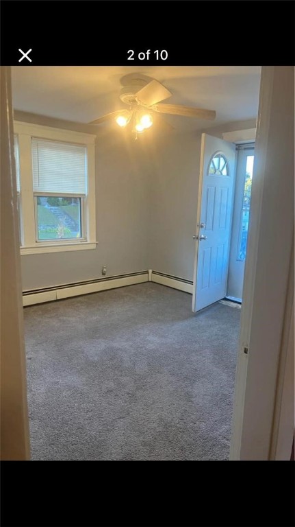 carpeted empty room featuring ceiling fan, a healthy amount of sunlight, and a baseboard radiator