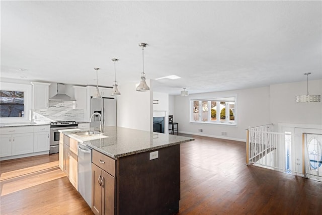 kitchen featuring pendant lighting, white cabinetry, stainless steel appliances, light stone countertops, and wall chimney exhaust hood