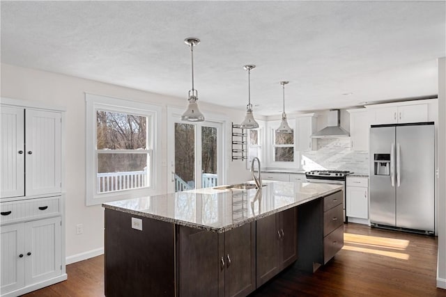 kitchen featuring wall chimney range hood, sink, white cabinetry, stainless steel appliances, and an island with sink