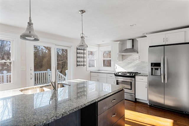 kitchen with pendant lighting, white cabinets, stainless steel appliances, light stone countertops, and wall chimney exhaust hood