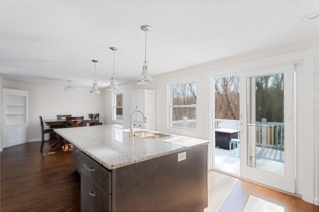 kitchen with pendant lighting, sink, dark hardwood / wood-style flooring, dark brown cabinets, and a center island with sink