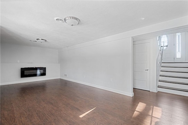 unfurnished living room with a textured ceiling and dark hardwood / wood-style flooring