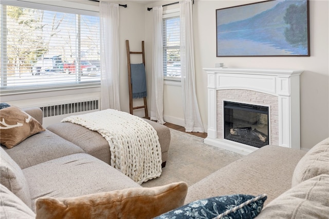 bedroom with hardwood / wood-style flooring, radiator heating unit, a stone fireplace, and multiple windows