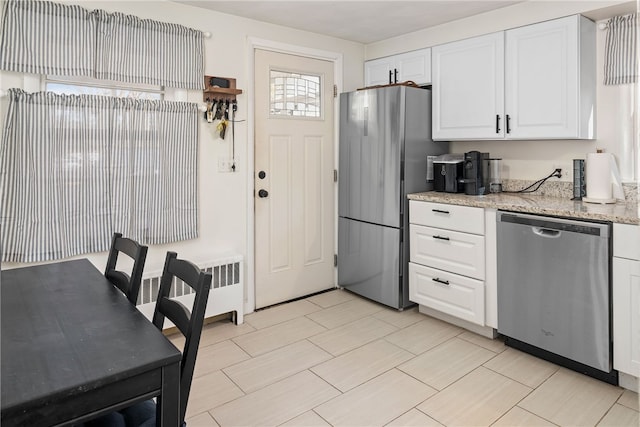 kitchen with white cabinetry, stainless steel appliances, light stone countertops, and radiator heating unit