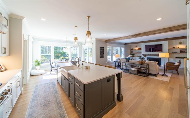 kitchen featuring sink, a kitchen island with sink, light wood-type flooring, and decorative light fixtures