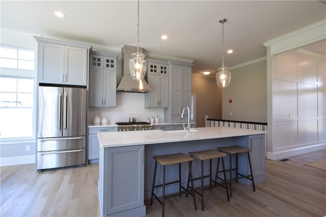 kitchen with wall chimney exhaust hood, an island with sink, high end refrigerator, and sink