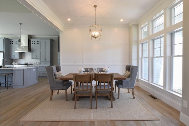 dining space featuring crown molding, an inviting chandelier, sink, and light hardwood / wood-style floors