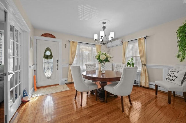 dining space with wood-type flooring, an AC wall unit, a healthy amount of sunlight, and an inviting chandelier