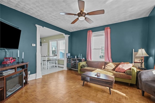 living room with ceiling fan, light parquet floors, decorative columns, and a textured ceiling