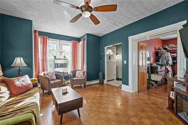 living room featuring baseboard heating, ceiling fan, parquet floors, and a textured ceiling