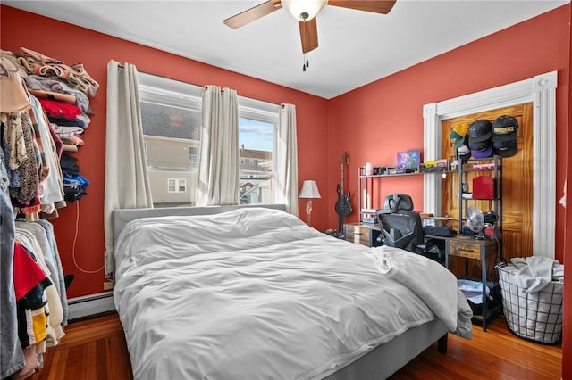 bedroom with ceiling fan, wood-type flooring, and a baseboard radiator