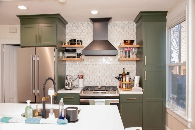 kitchen with sink, green cabinetry, appliances with stainless steel finishes, wall chimney range hood, and backsplash