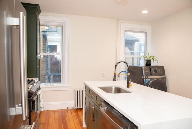 kitchen with sink, a center island with sink, light wood-type flooring, appliances with stainless steel finishes, and radiator