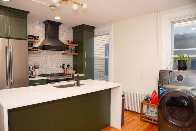 kitchen featuring light wood-type flooring, radiator, green cabinets, washer / clothes dryer, and wall chimney range hood