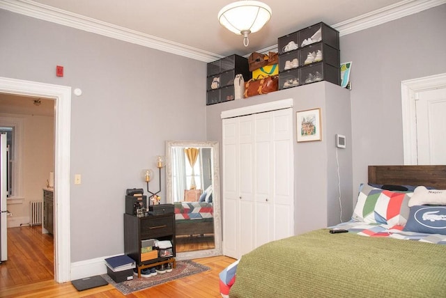 bedroom featuring hardwood / wood-style flooring, radiator heating unit, ornamental molding, and a closet