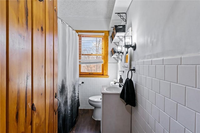 bathroom with toilet, a textured ceiling, tile walls, vanity, and hardwood / wood-style floors