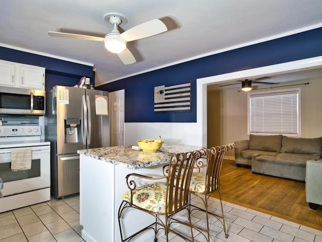 kitchen with light stone counters, light tile patterned floors, appliances with stainless steel finishes, a kitchen breakfast bar, and white cabinets