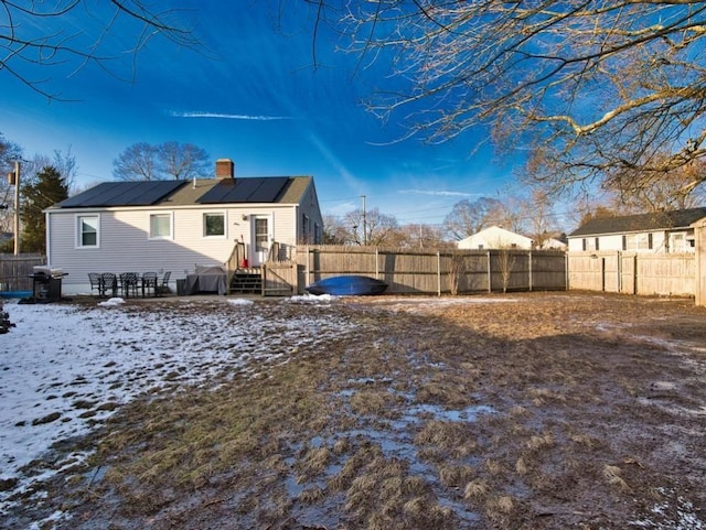 snow covered rear of property featuring solar panels