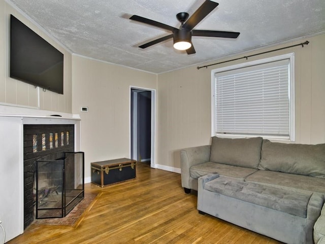 living room with a fireplace, wood-type flooring, ornamental molding, ceiling fan, and a textured ceiling