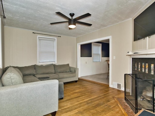 living room with a textured ceiling, wood-type flooring, ornamental molding, and ceiling fan