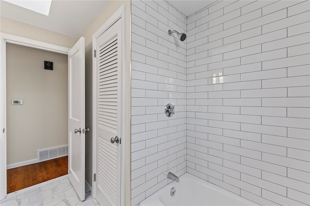 bathroom with a skylight and tiled shower / bath combo