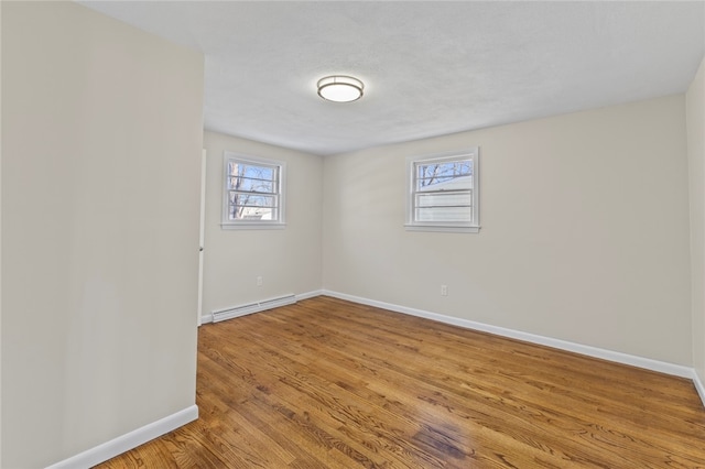 spare room with a healthy amount of sunlight, baseboard heating, and light hardwood / wood-style floors