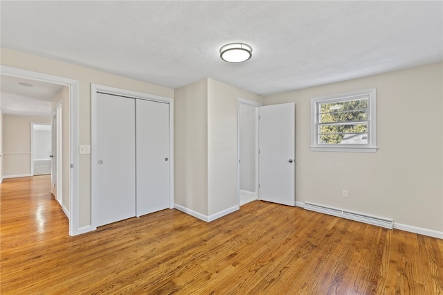 unfurnished bedroom with light wood-type flooring, a closet, and baseboard heating