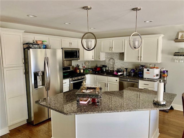 kitchen with stainless steel appliances, sink, dark stone counters, and decorative light fixtures