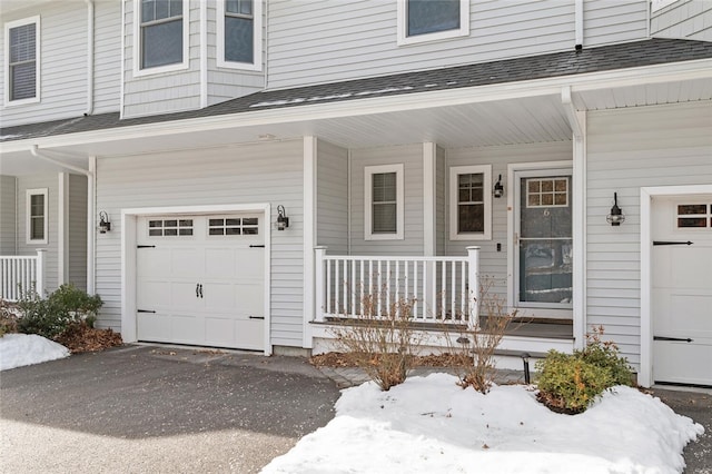 snow covered property entrance featuring a garage and a porch