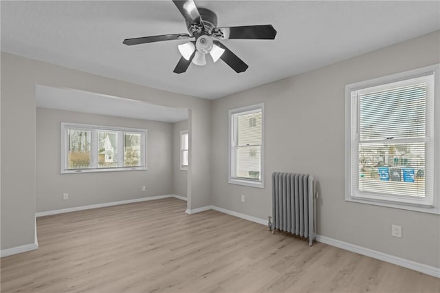 empty room with a wealth of natural light, radiator heating unit, and light wood-type flooring